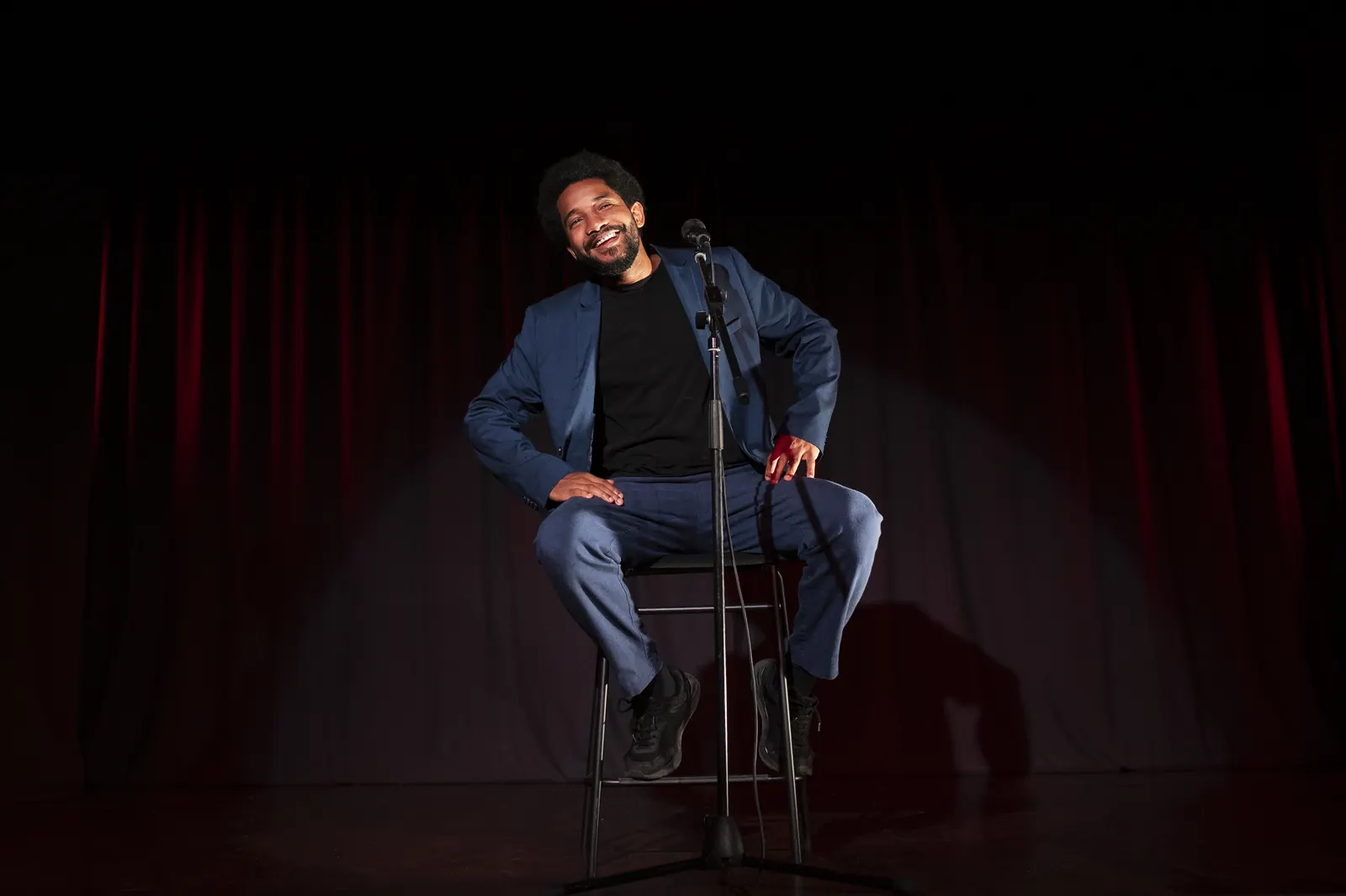 Stand-up-Comedian mit Mikrofon auf einer Bühne vor rotem Vorhang